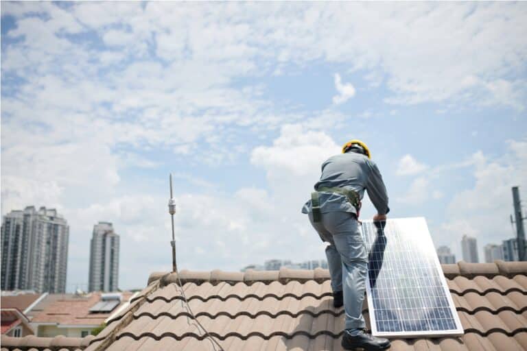worker in hardhat and grey uniform installing solar panel on roof