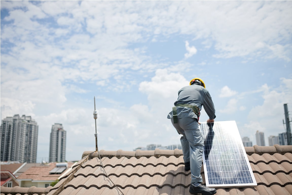 worker in hardhat and grey uniform installing solar panel on roof